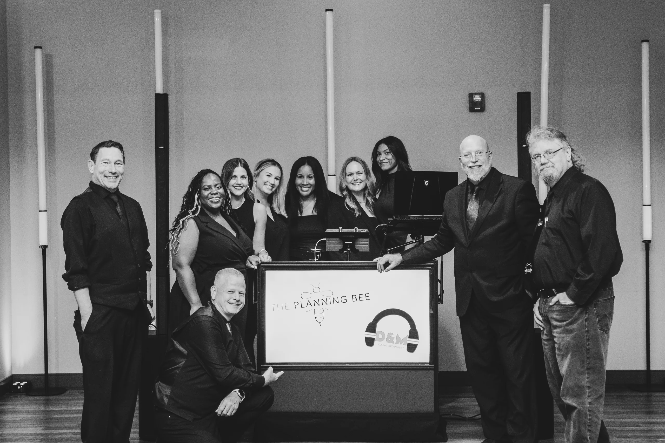 The D&M DJ Entertainment and The Planning Bee teams standing around a DJ booth showing both logos